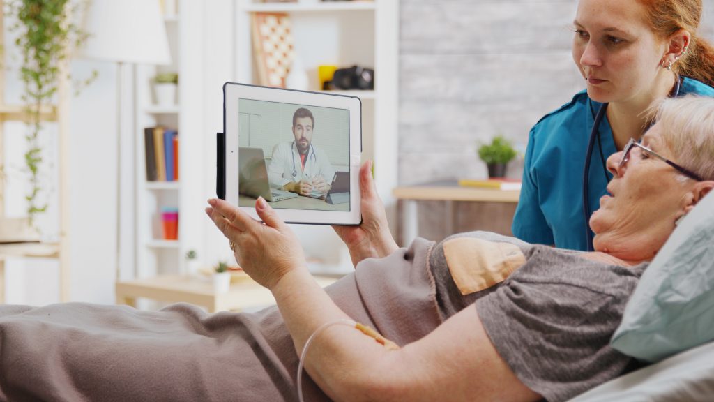 Old woman lying in hospital bed having an online video call with a doctor