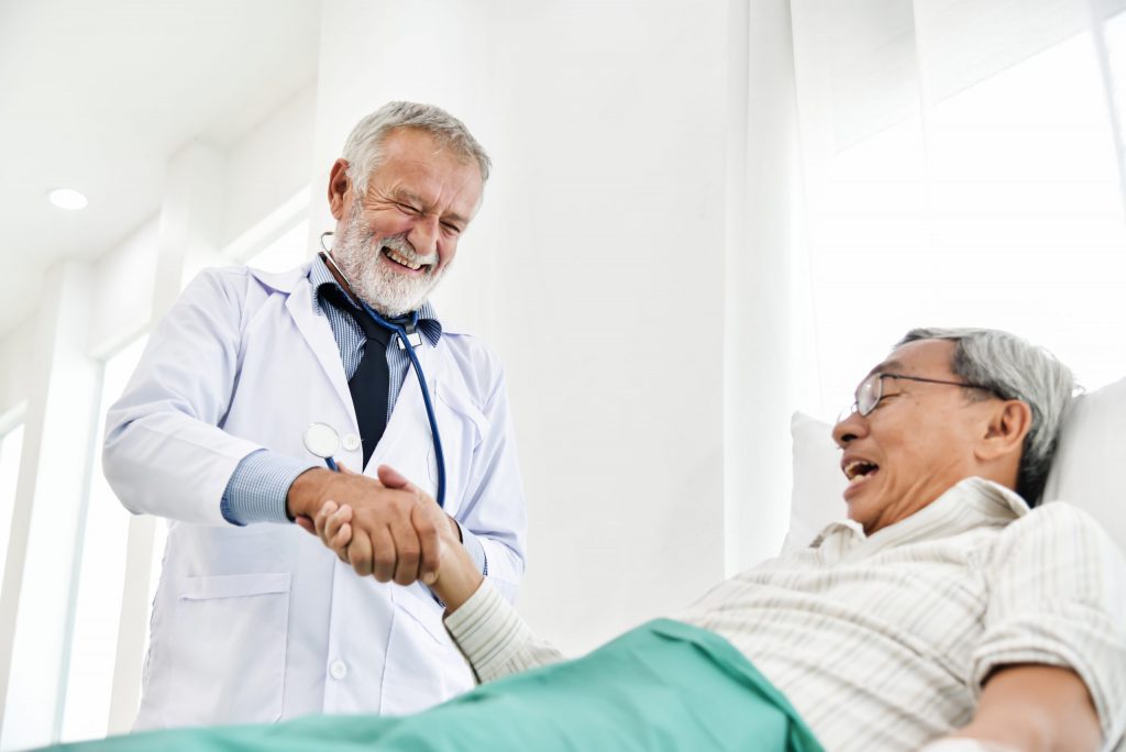 Happy male doctor hand shaking and discussing with senior patient